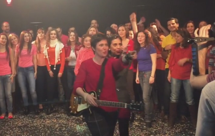 Una de ellas con guitarra eléctrica canta rodeada de figurantes durante el rodaje de «Juego de maletas»