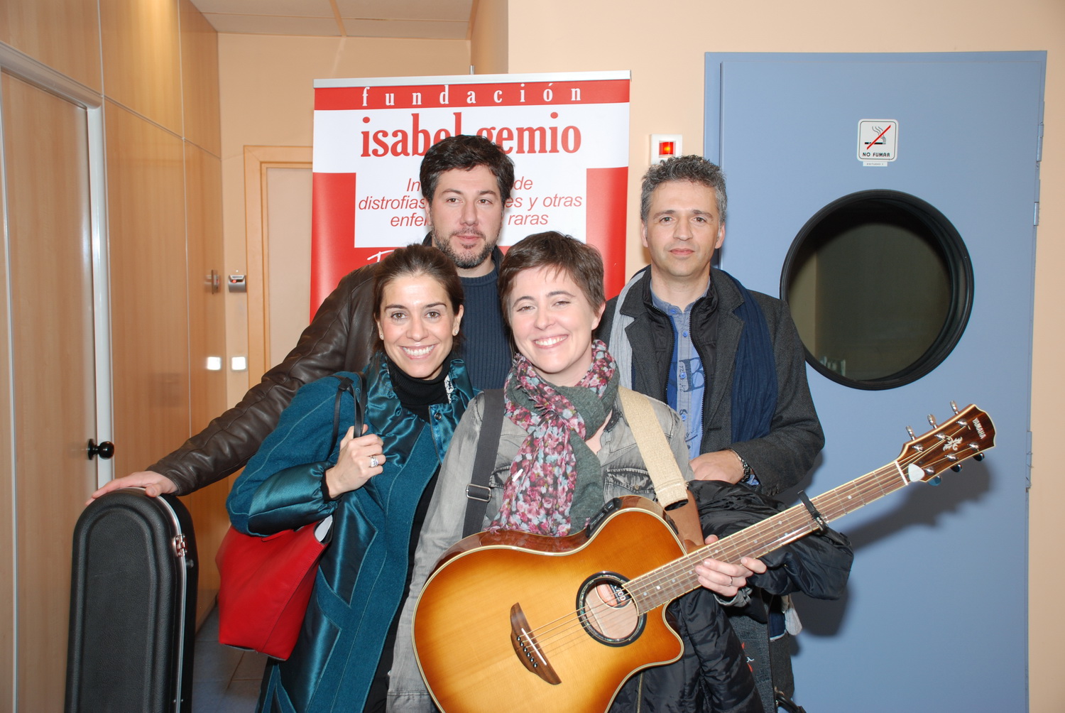 Ana y Susana con una guitarra junto a dos compañeros ante un cartel de la Fundación Isabel Gemio